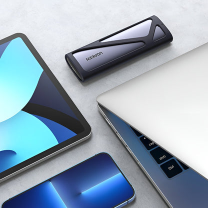 Tablet, smartphone, and laptop on a light gray surface with a Ugreen M.2 external enclosure in the center.