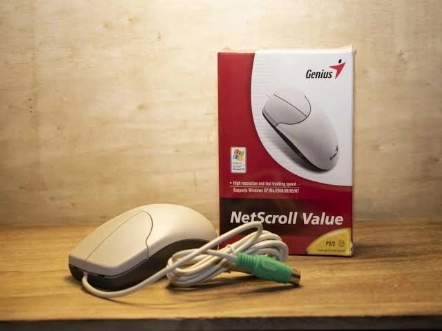 White computer mouse with cable and Genius NetScroll Value box on a wooden surface