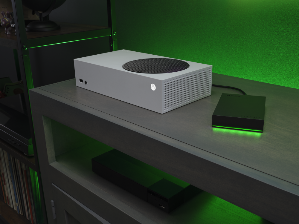 Seagate Xbox Game Drive 2TB (STKX2000400) connected to an Xbox Series S console — stylish black external hard drive with glowing green LED base, placed on a modern gaming setup shelf, expanding storage for Xbox gaming.