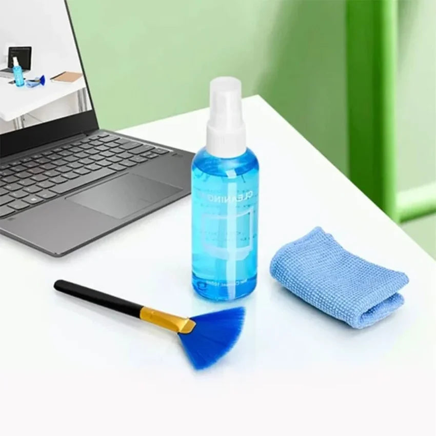 Cleaning tools including a spray bottle, brush, and cloth on a desk with a laptop in the background.